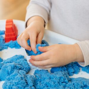 Child engaging with kinetic sand during sensory play, focusing on tactile exploration and sensory integration, highlighting hands-on and therapeutic occupational therapy services.